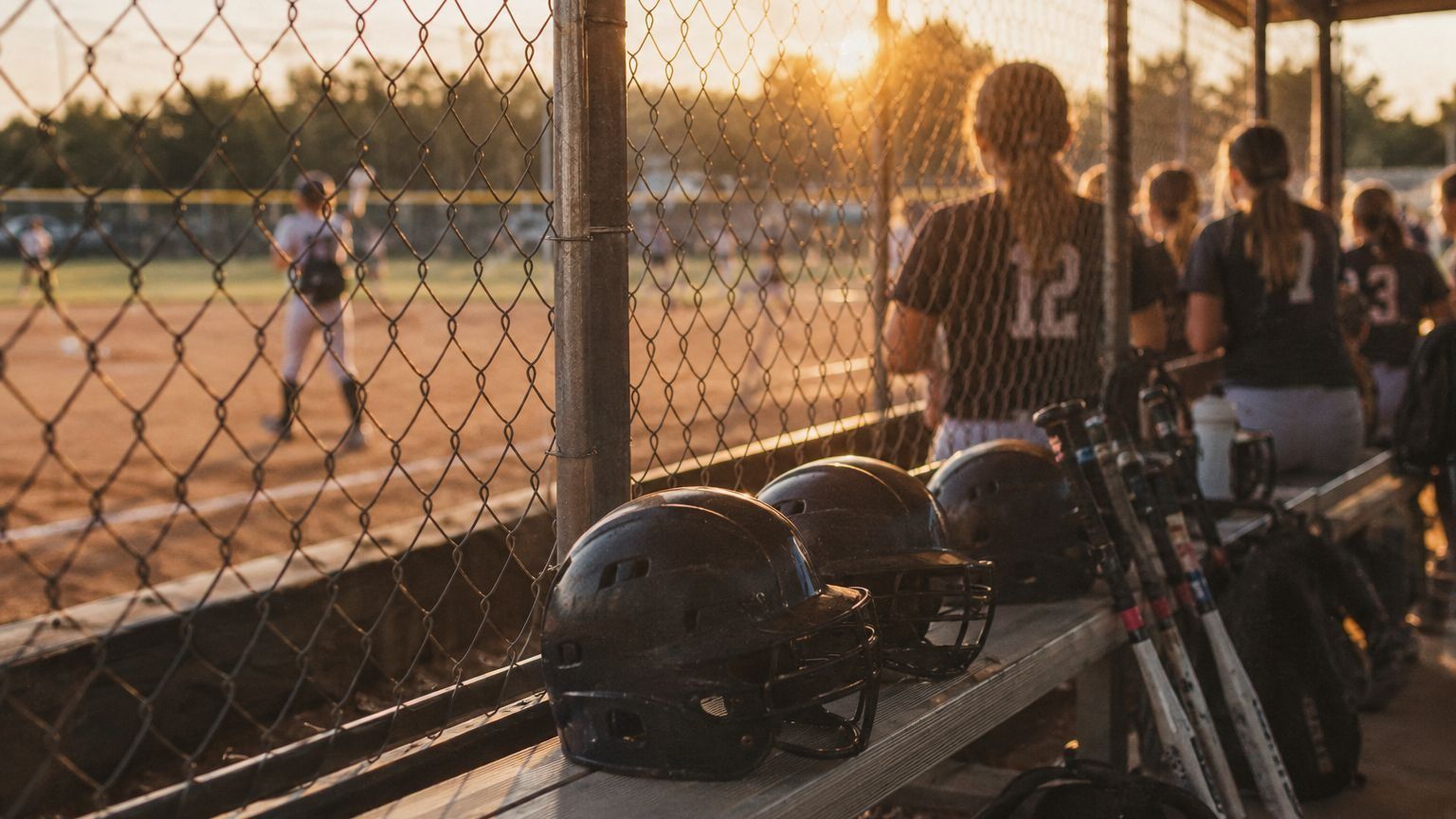Teammates watch the game together from the dugout at golden hour.